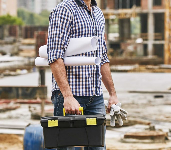 Everything what i need for work. Cropped image of a builder holding toolbox, protectives gloves and engineering drawings while standing at construction site. Building concept. Protective gear. Construction concept